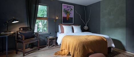A bedroom with a bed, a desk, a chair, a window, and a painting on the wall.