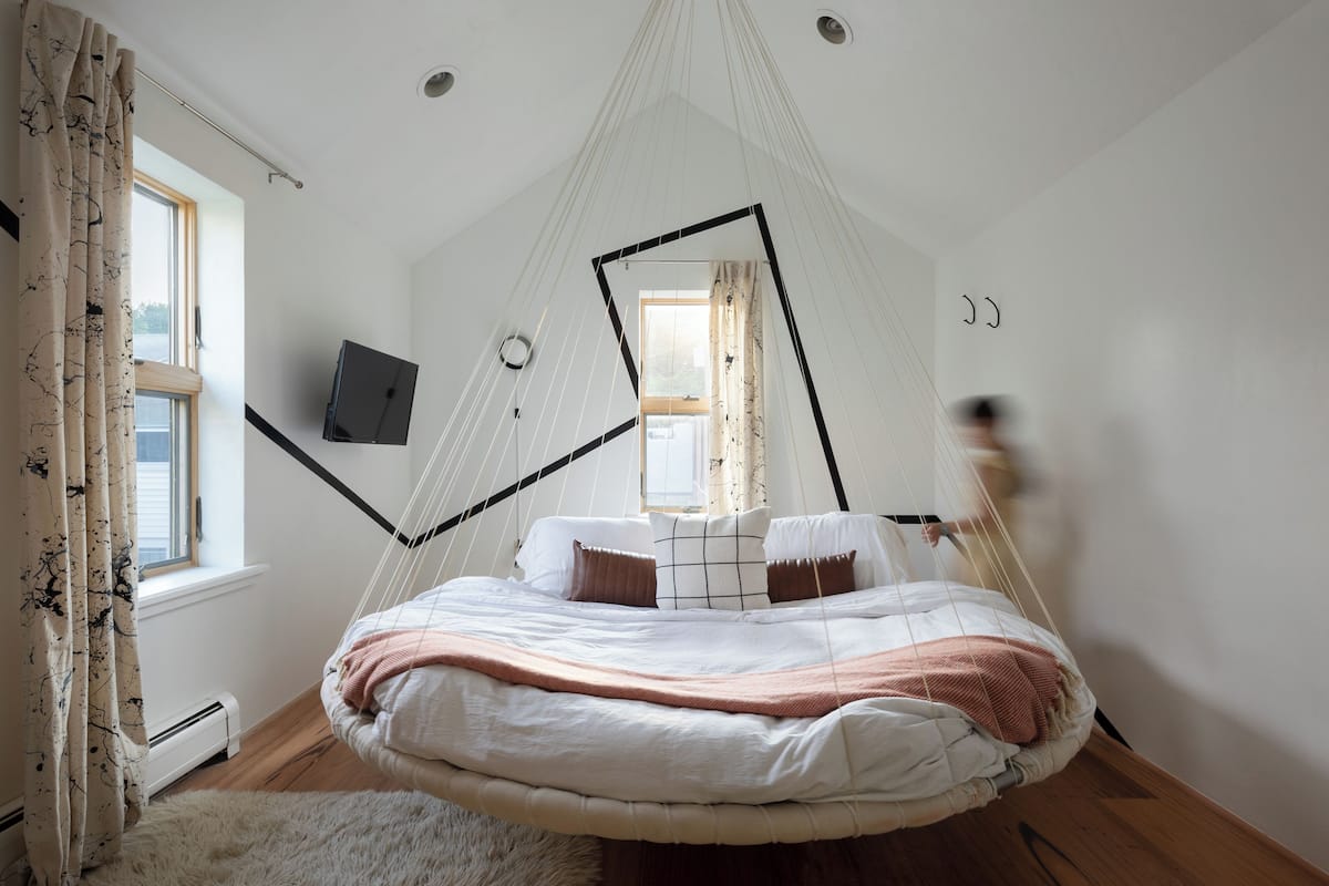 A room with a hanging bed, a white wall, a window, and a door.