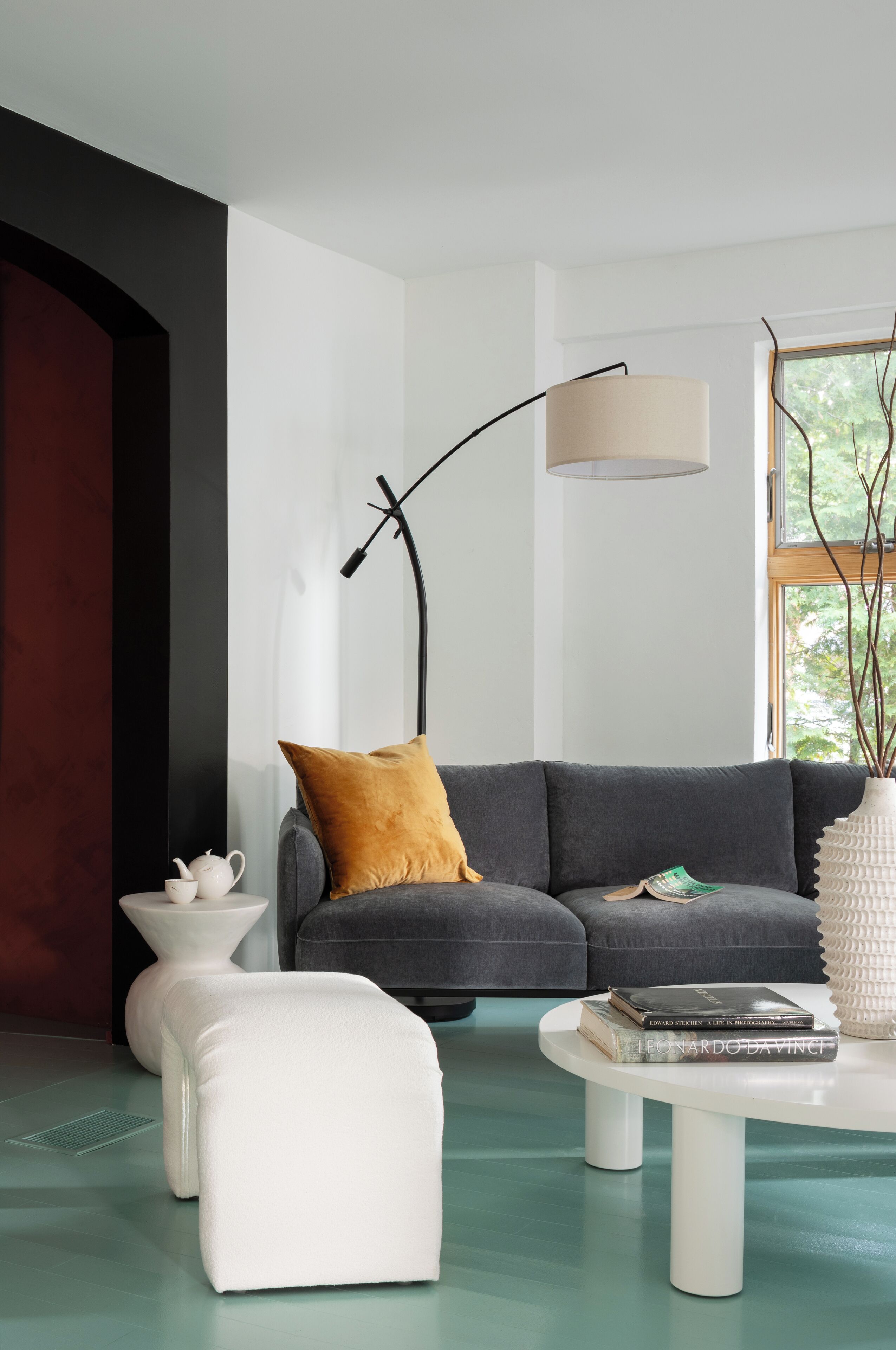 Una sala de estar moderna con un sofá gris, un otoman blanco, una mesita de centro blanca y una lámpara de pie.