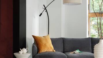 Una sala de estar moderna con un sofá gris, un otoman blanco, una mesita de centro blanca y una lámpara de pie.