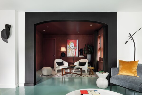 A modern living room with a dark archway, two white armchairs, a grey sofa, a round coffee table, and a floor lamp.