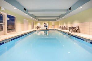 A swimming pool with clear blue water, surrounded by chairs and tables, and a door leading outside. - Holiday Inn Express & Suites Great Bend by IHG (Great Bend)