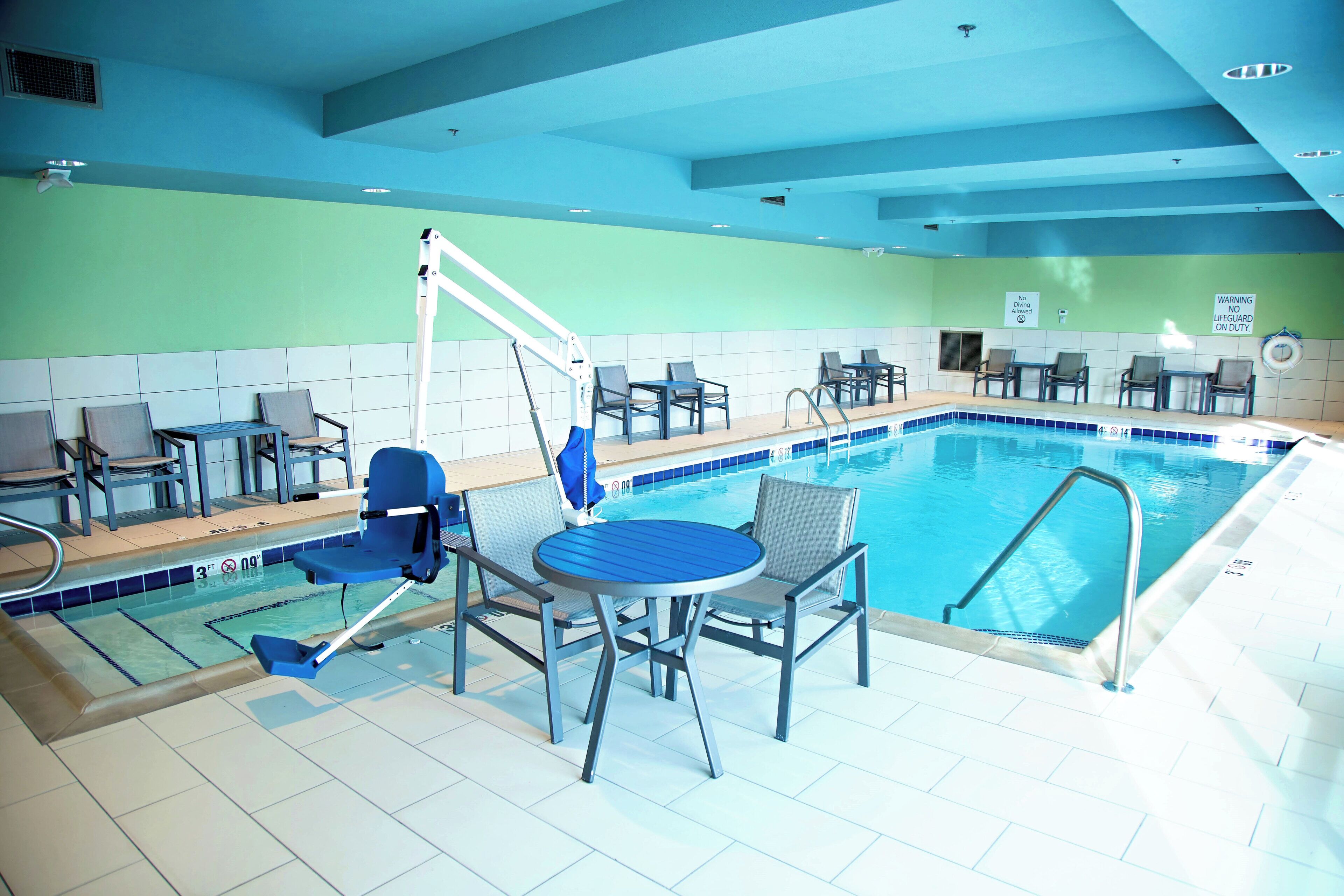 An indoor swimming pool with a diving board, lounge chairs, and a lifeguard sign.
