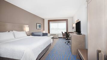 A hotel room with a large bed, a desk, a chair, a television, and a window with a city view.