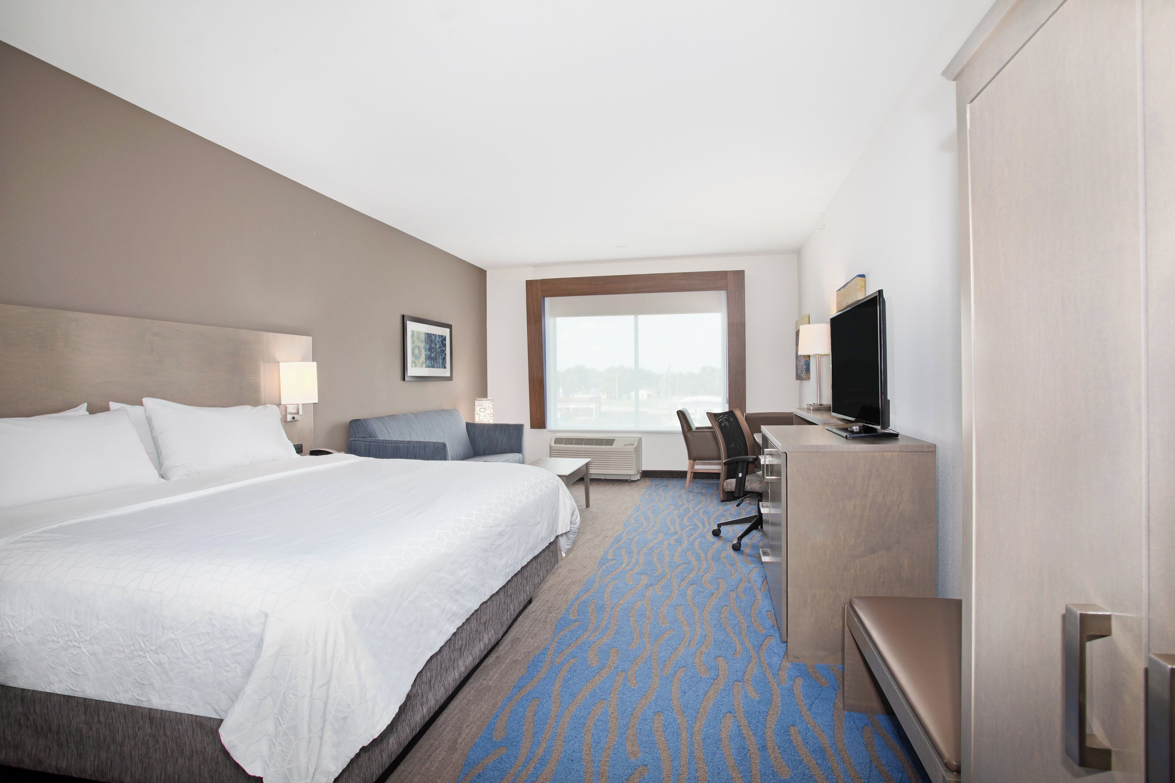 Une chambre d’hôtel avec un grand lit, un bureau avec une chaise, une télévision et une fenêtre donnant sur un beau paysage.