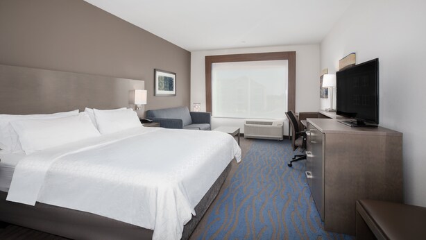 Ein Hotelzimmer mit einem großen Bett, einem Schreibtisch mit Fernseher, einem Sessel und einem Fenster mit Aussicht.