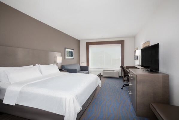 Habitación de hotel con una cama grande, un escritorio con televisor, una silla y una ventana con vistas.