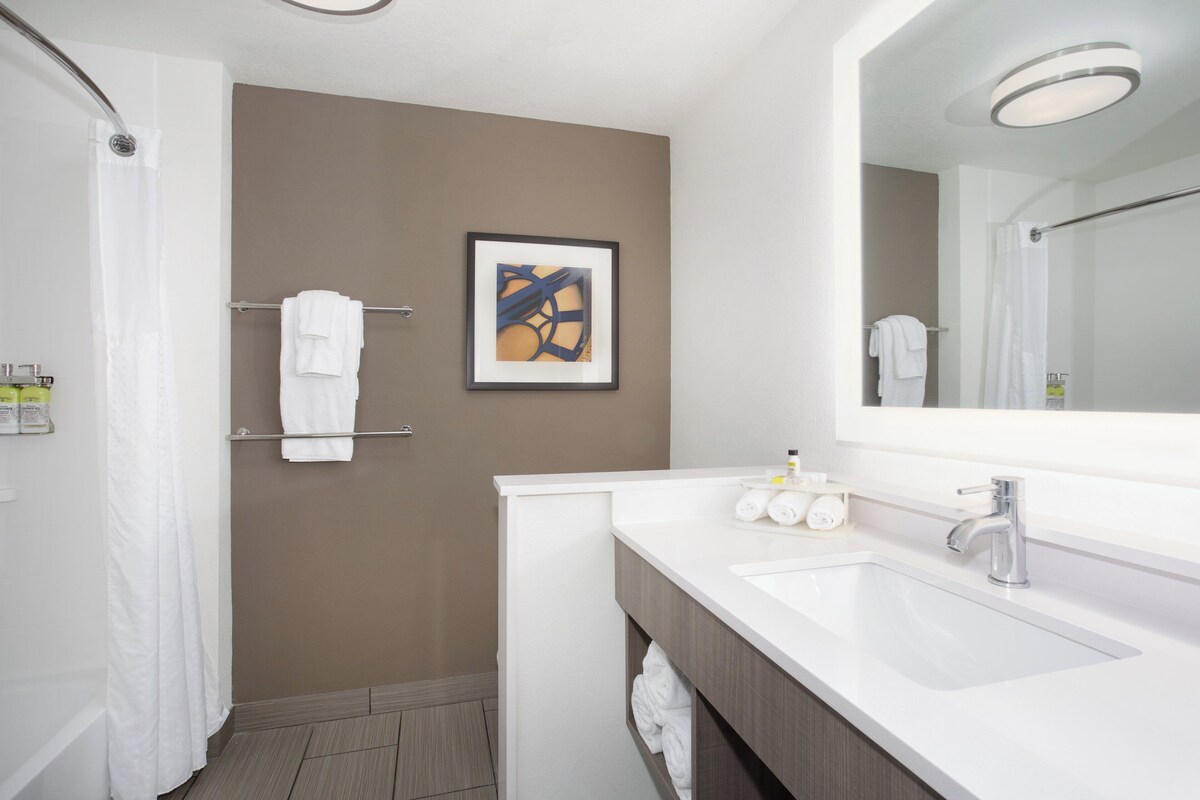 Un baño moderno con un lavamanos blanco, un espejo grande, una cortina de ducha y un perchero para toallas.
