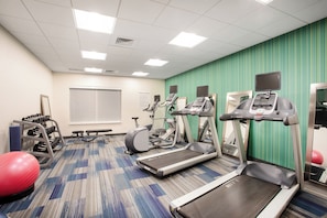 A fitness center with treadmills, elliptical machines, and a wall-mounted screen.