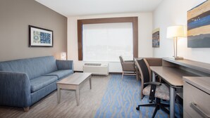 Ein Hotelzimmer mit einem blauen Sofa, einem Schreibtisch, einem Stuhl, einer Lampe und einem großen Fenster.