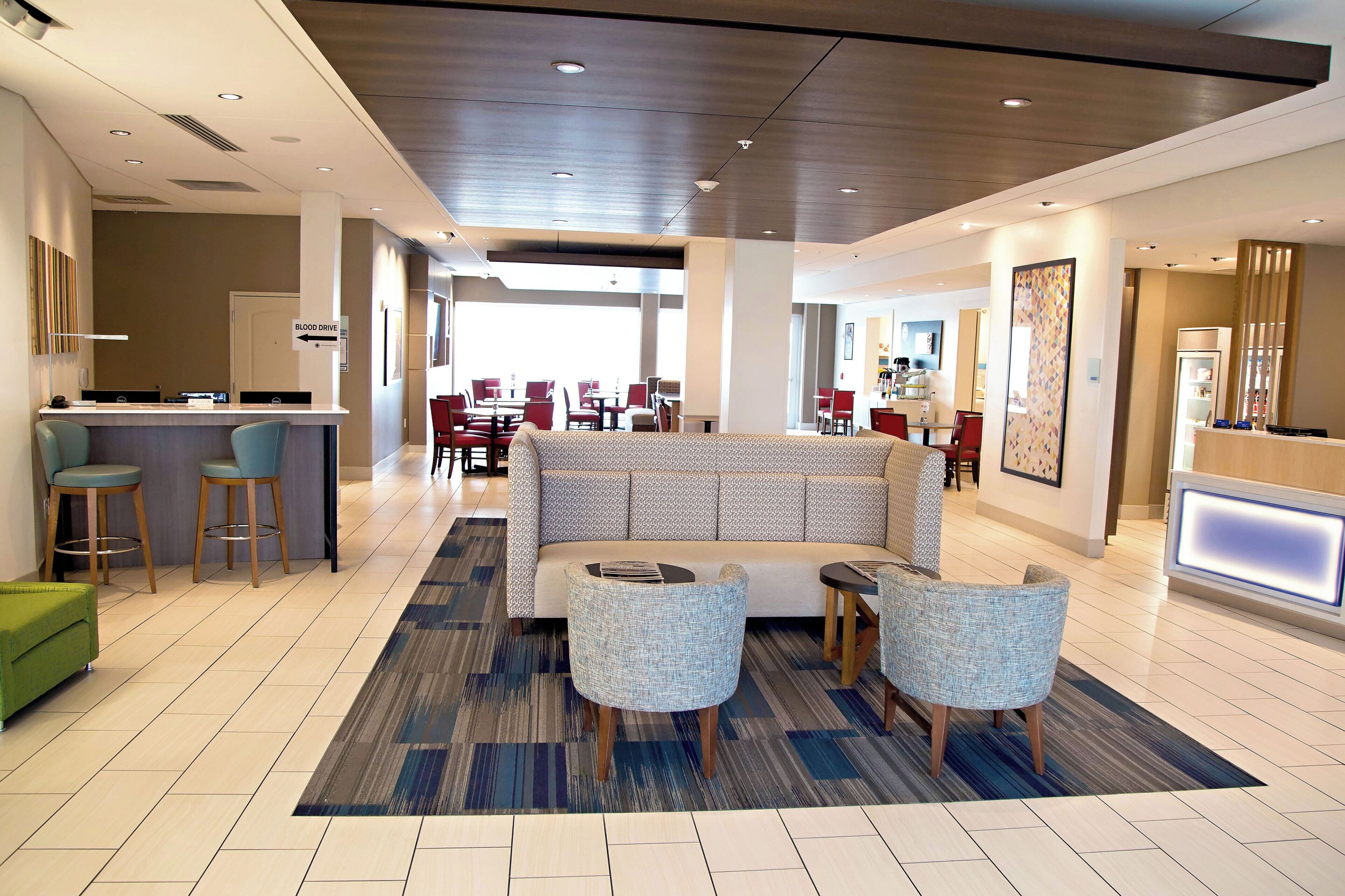 Un vestíbulo de hotel con una recepción, una zona de estar con sofá y sillones, y un bar.