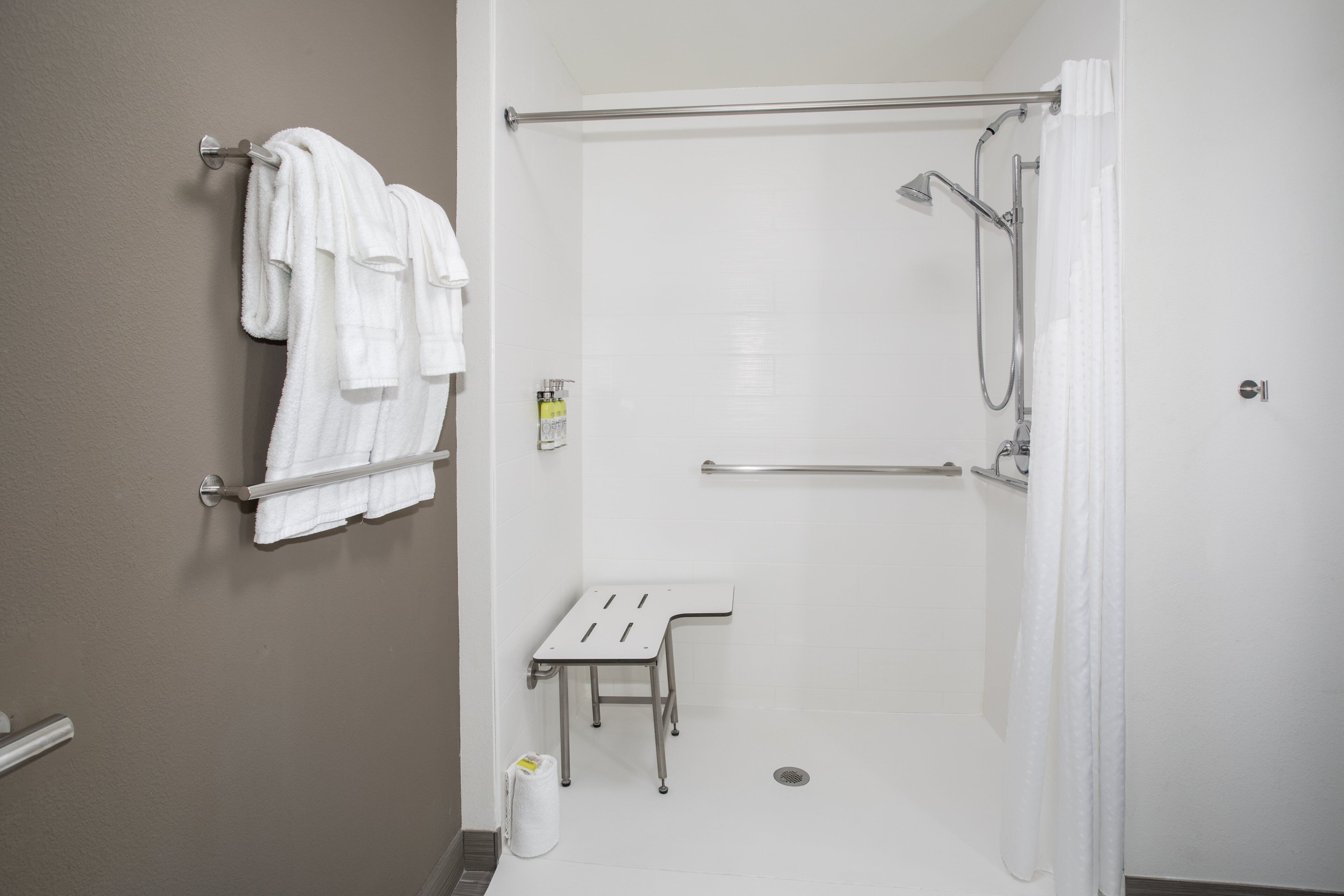 A bathroom with a shower, a towel rack with multiple towels, a small table, and a toilet paper dispenser.