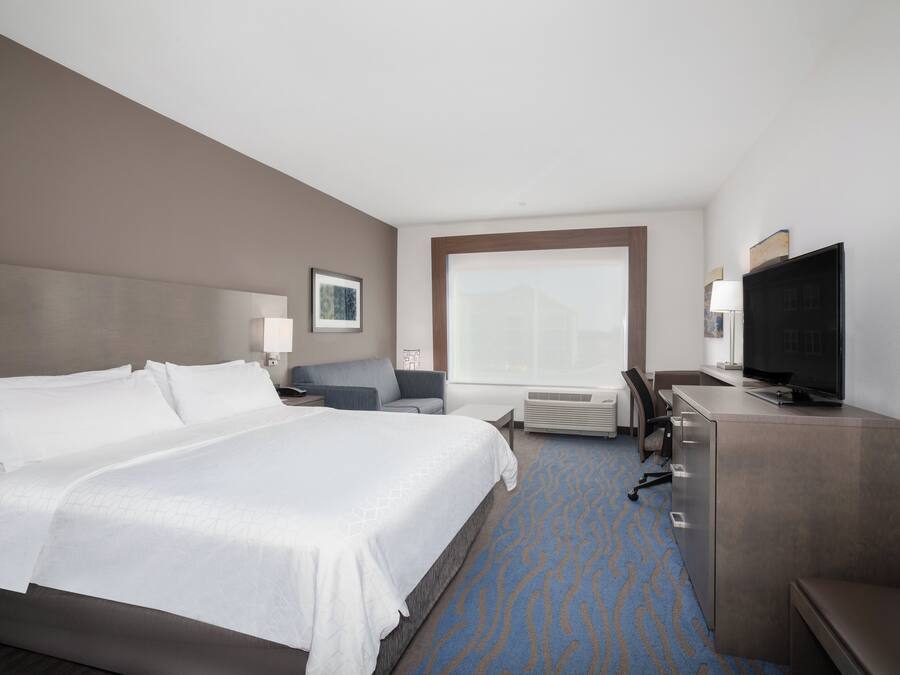 A hotel room with a large bed, a desk, a television, and a window.