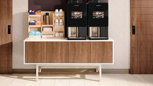 Eine Kaffeestation mit zwei Kaffeeautomaten, einer Kaffeemühle und verschiedenen Kaffeuzubehörteilen auf Regalen.