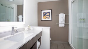 Ein modernes Badezimmer mit einem großen Spiegel, einem weißen Waschbecken und einer Duschkabine aus Glas.