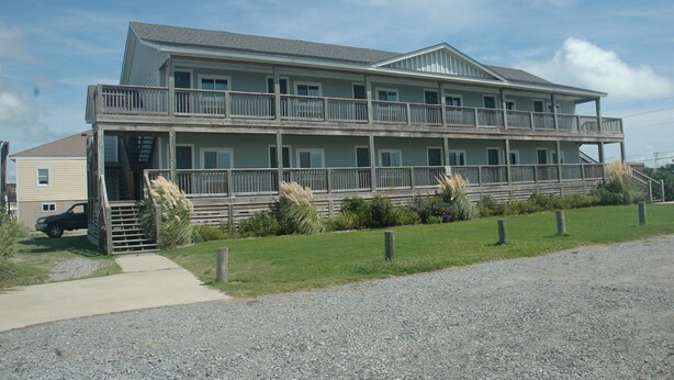 A two-story building with a balcony on the upper floor, a covered front porch, and a gravel driveway. - Village Marina (Hatteras)