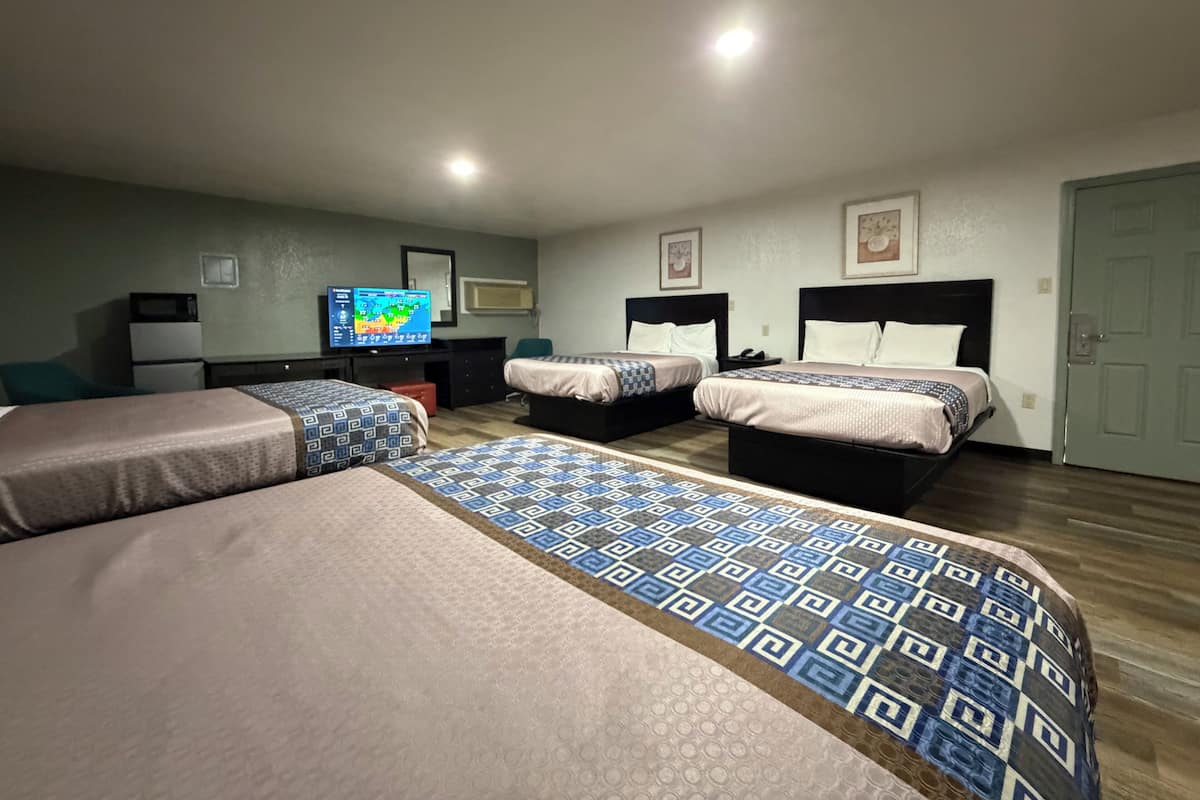 A hotel room with two beds, a desk with a computer, a TV, and a door.