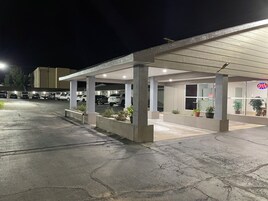 Um estacionamento com área externa coberta, um edifício com placa indicando que está aberto e vários carros estacionados.