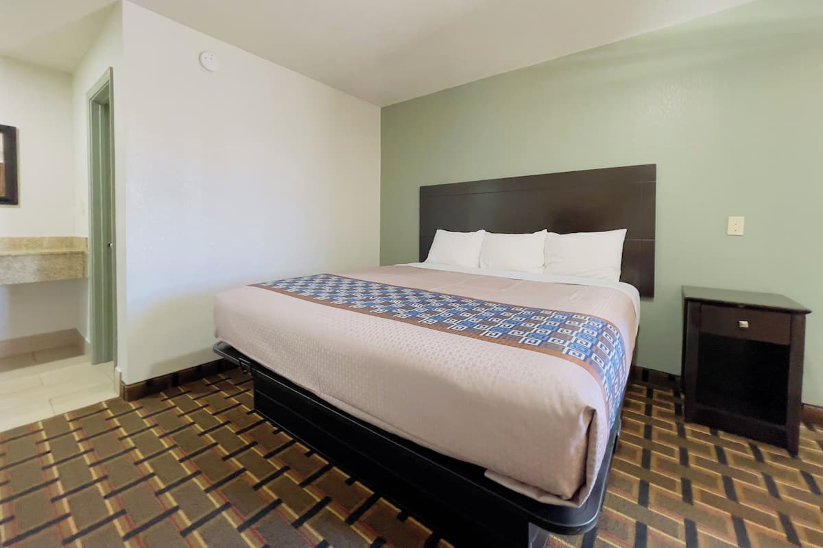 A hotel room with a bed, a nightstand, a bathroom with a sink, and a patterned floor.
