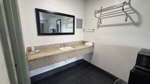 A bathroom with a granite countertop, a sink, a mirror, a towel rack, and a trash bin. - Budget Inn (Ada)