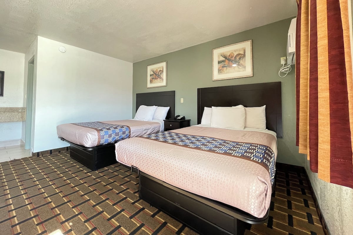 A hotel room with two beds, a patterned carpet, and a painting on the wall.