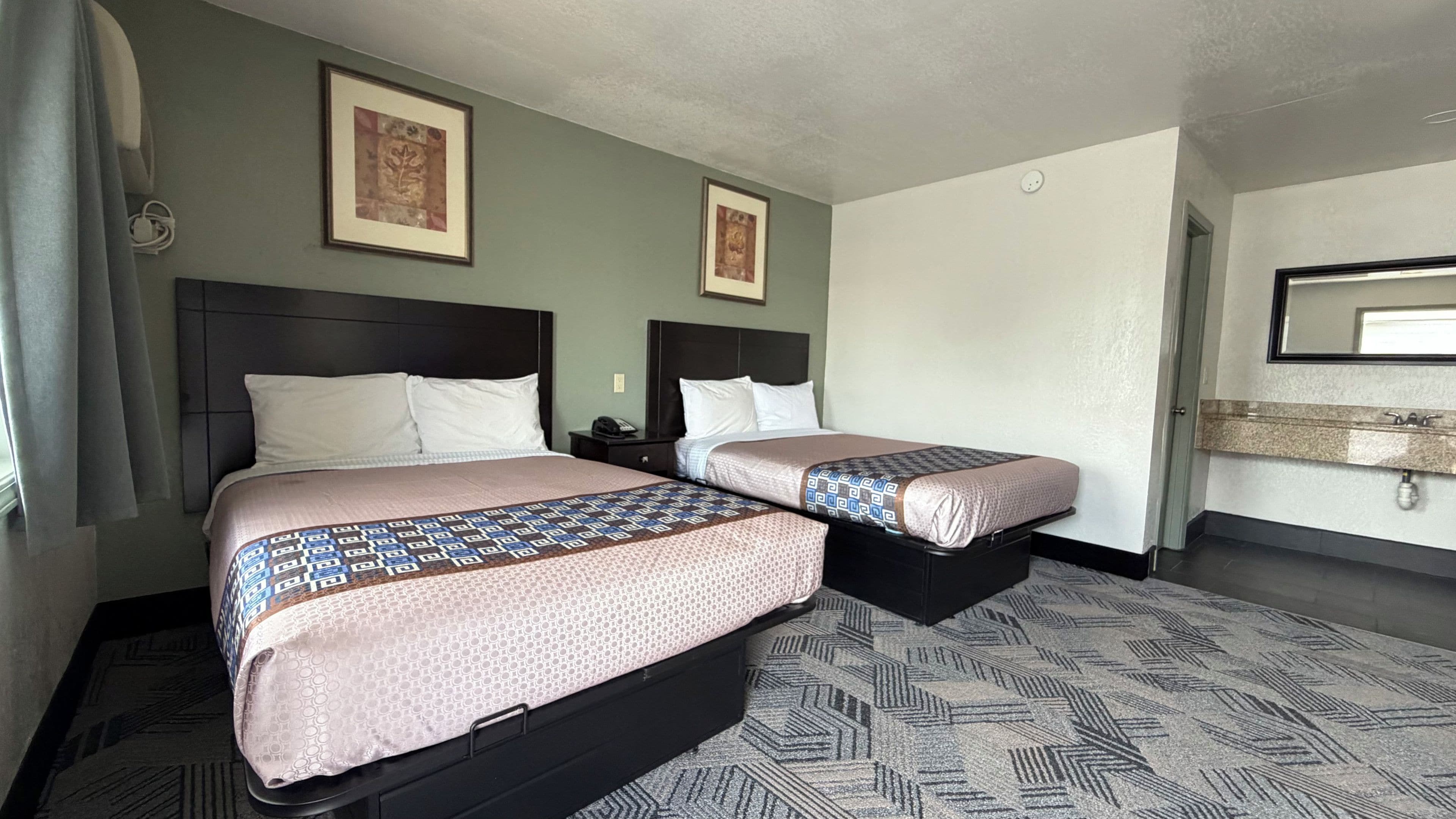 A hotel room with two beds, a nightstand, a mirror, and a wall-mounted light fixture.