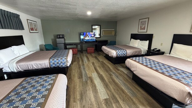 A hotel room with two beds, a desk, a television, and a small kitchenette. - Budget Inn (Ada)