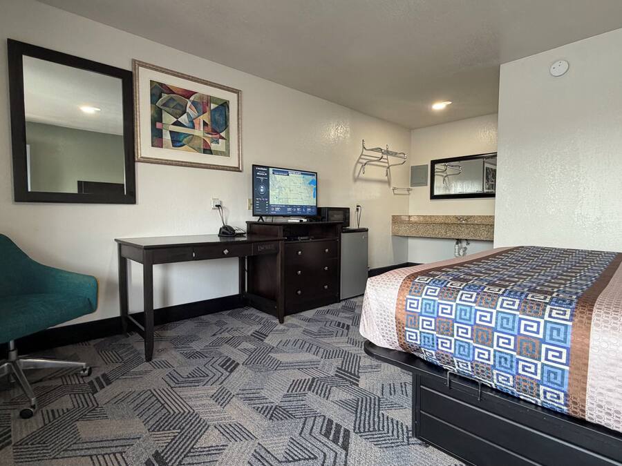 Habitación de hotel con cama, escritorio, silla, televisor y un cuadro en la pared.