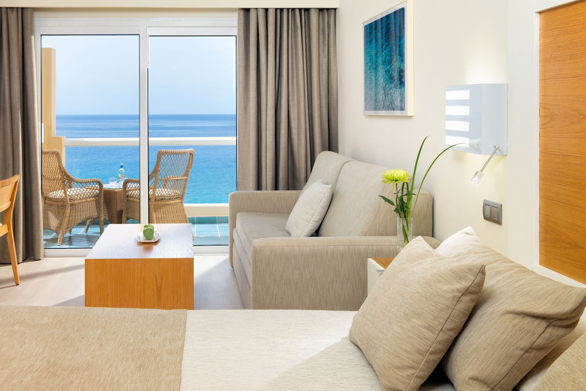 A modern hotel room with a sofa, a dining table, and a view of the ocean.