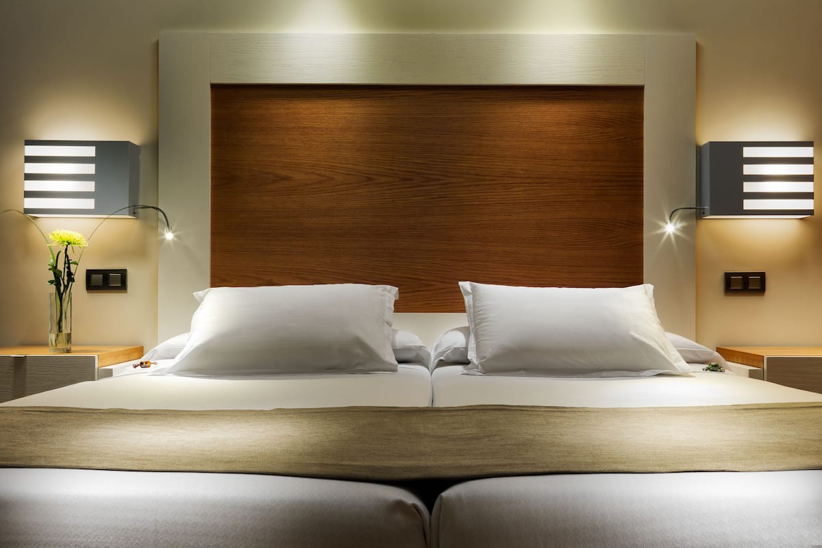 A modern hotel room with a large bed, wooden headboard, bedside lamps, and a vase with flowers.