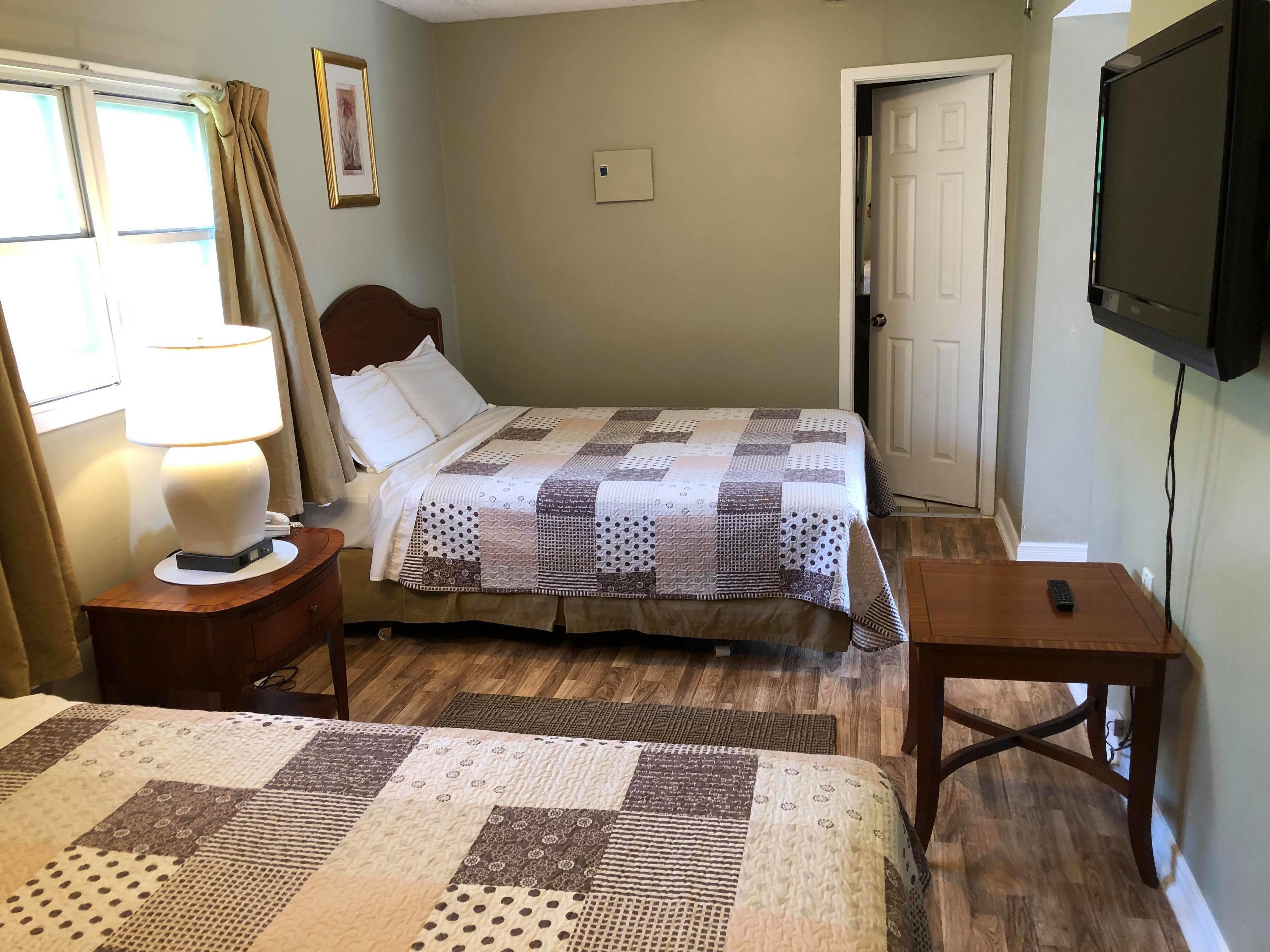 A bedroom with two beds, a bedside table with a lamp, a TV on the wall, and a door.