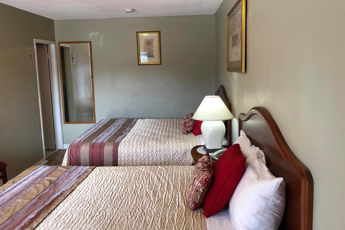A hotel room with two beds, a nightstand with a lamp, and a framed picture on the wall.