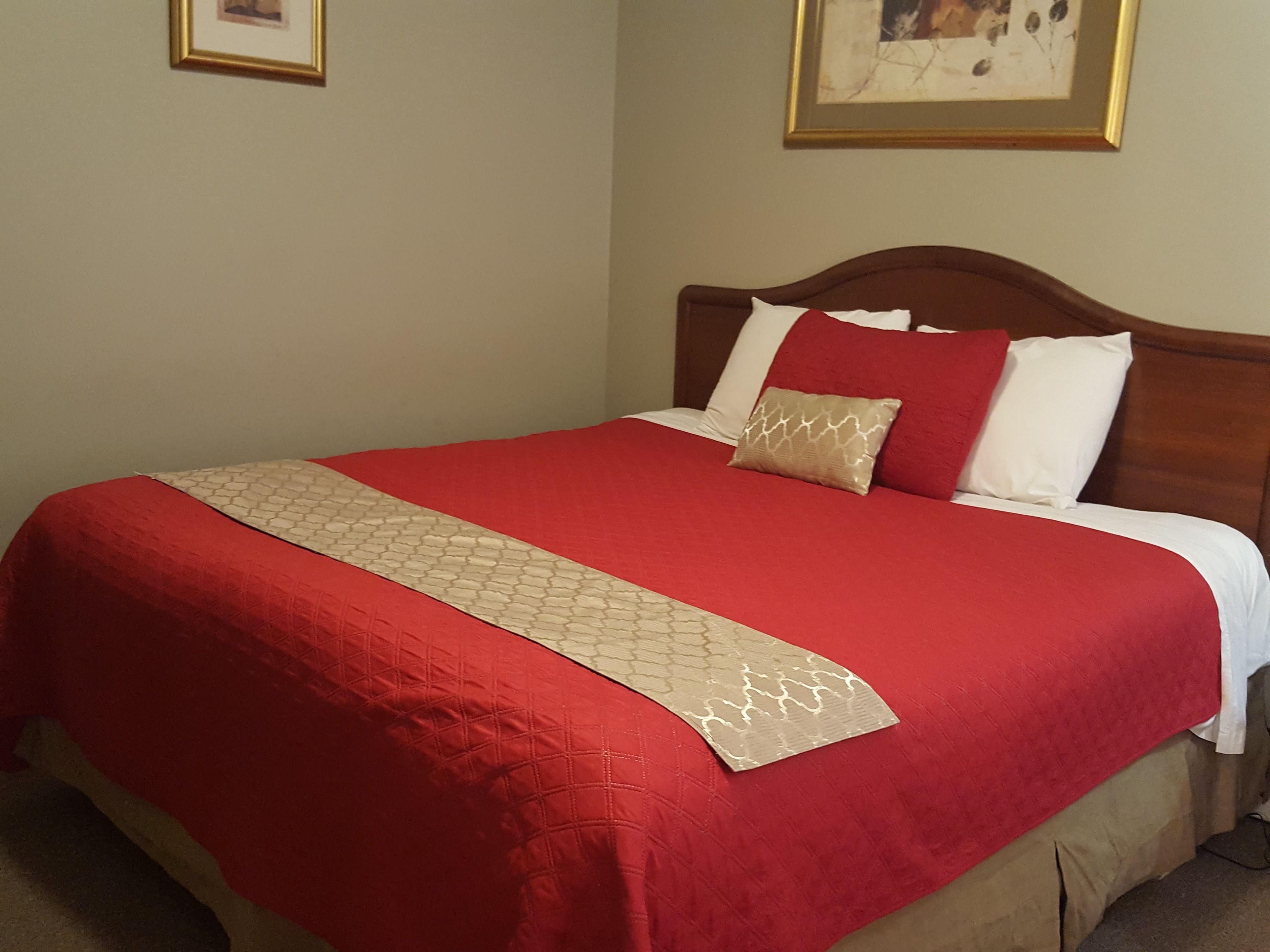 A neatly made bed with a red and beige bedspread, a wooden headboard, and two pillows.