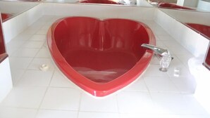 A heart-shaped bathtub in a bathroom with white tiles and a glass shower enclosure. - Niagara Inn & Suites (Niagara Falls)