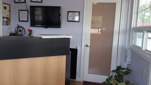 A kitchen with a black countertop, a television mounted on the wall, and a door with a frosted glass panel. - Niagara Inn & Suites (Niagara Falls)