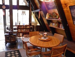 Ein gemütliches Zimmer mit Holztisch und -stühlen, einem Bücherregal und einem kleinen Herd.