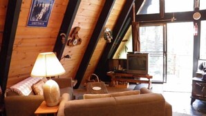 A cozy cabin interior with a wooden interior, a sofa, a table with a lamp, a television, and a poster on the wall. - 916 Kiowa (South Lake Tahoe)