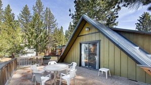 A wooden cabin with a sloped roof, a glass door, and a gravel patio with white chairs. - 890 Candlewood Drive (South Lake Tahoe)
