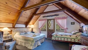 A cozy attic bedroom with two beds, a chair, and a television. - 890 Candlewood Drive (South Lake Tahoe)