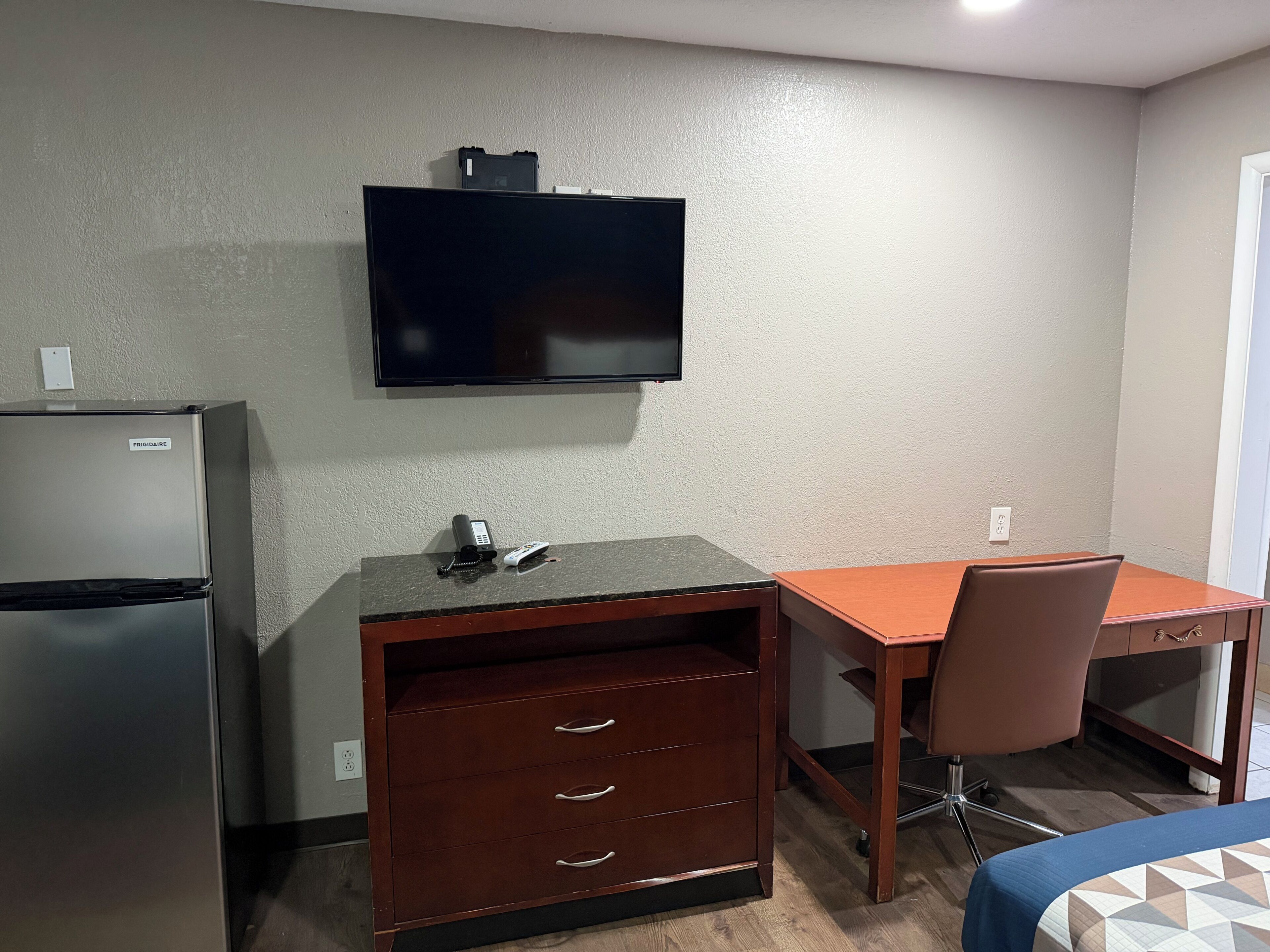 Een kleine hotelkamer met een kitchenette, een bureau, een stoel en een bed.