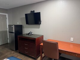 Una kitchenette compacta con refrigerador, microondas, una pequeña superficie de apoyo y televisión montada en la pared.