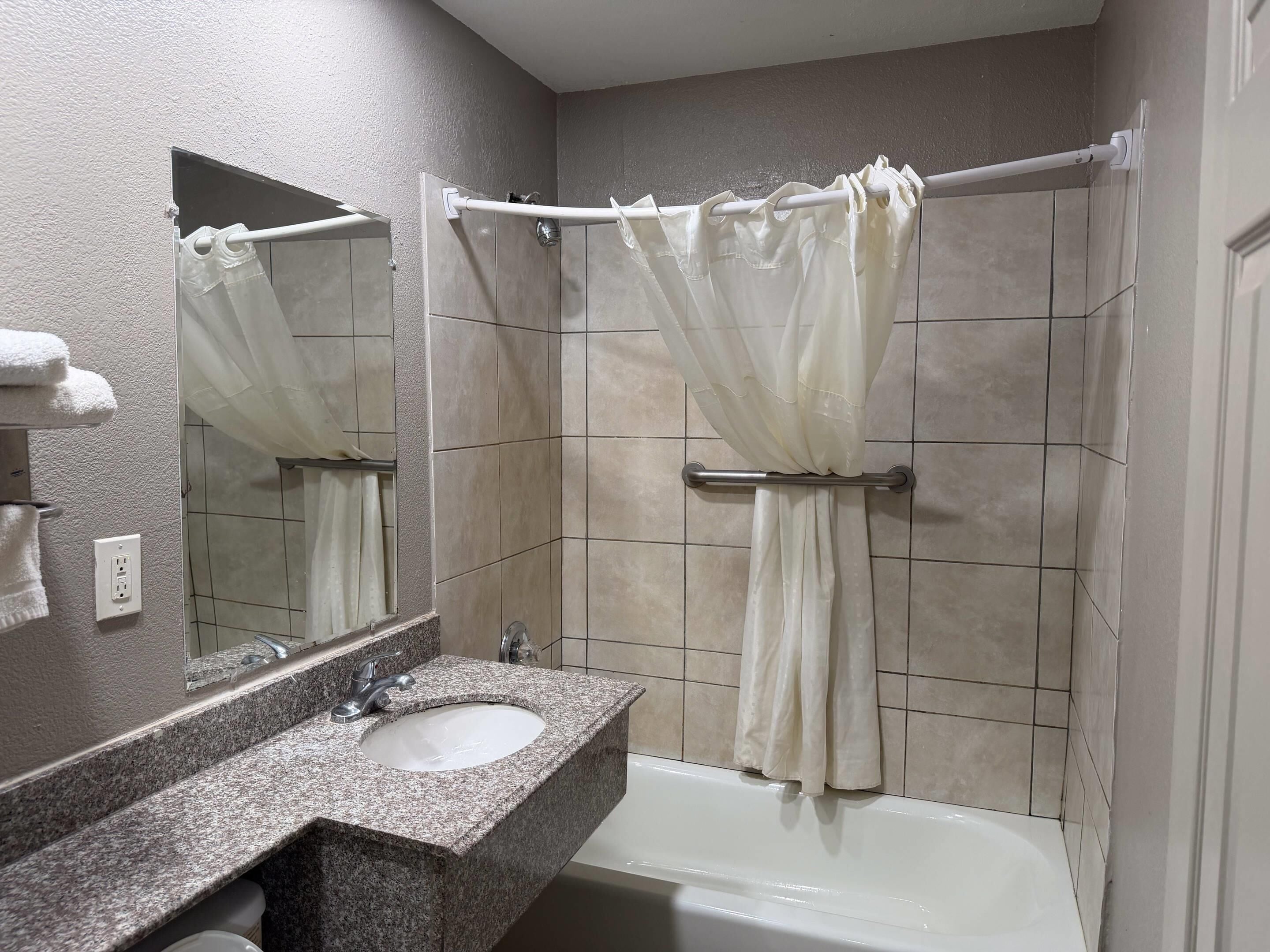 A bathroom with a granite countertop sink, a mirror, a shower with a curtain, and a bathtub.