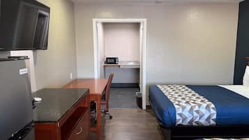 Una habitación pequeña con cama, escritorio, silla, televisor y refrigerador.
