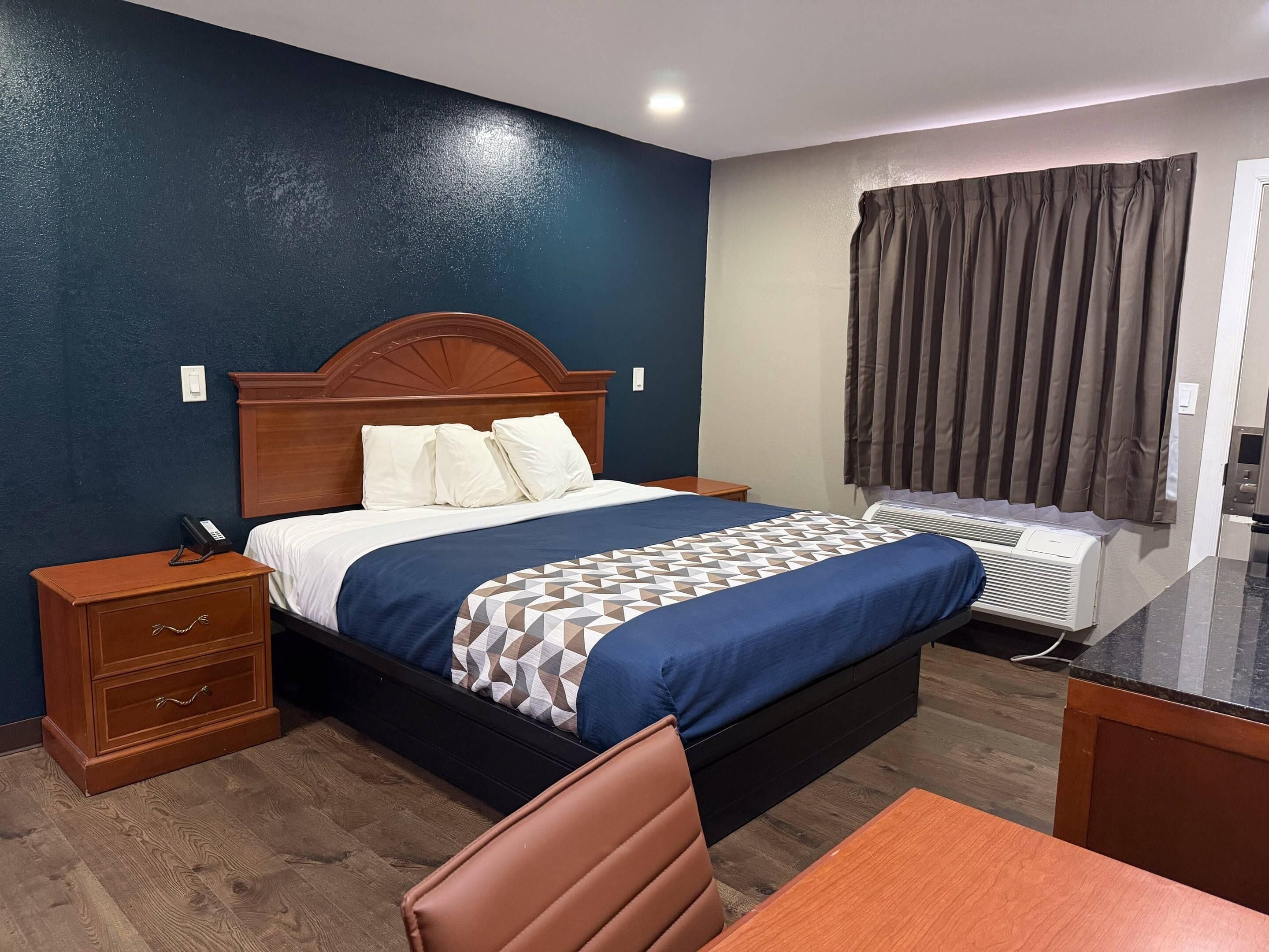 Una habitación de hotel con cama, mesita de noche, silla y equipo de aire acondicionado.