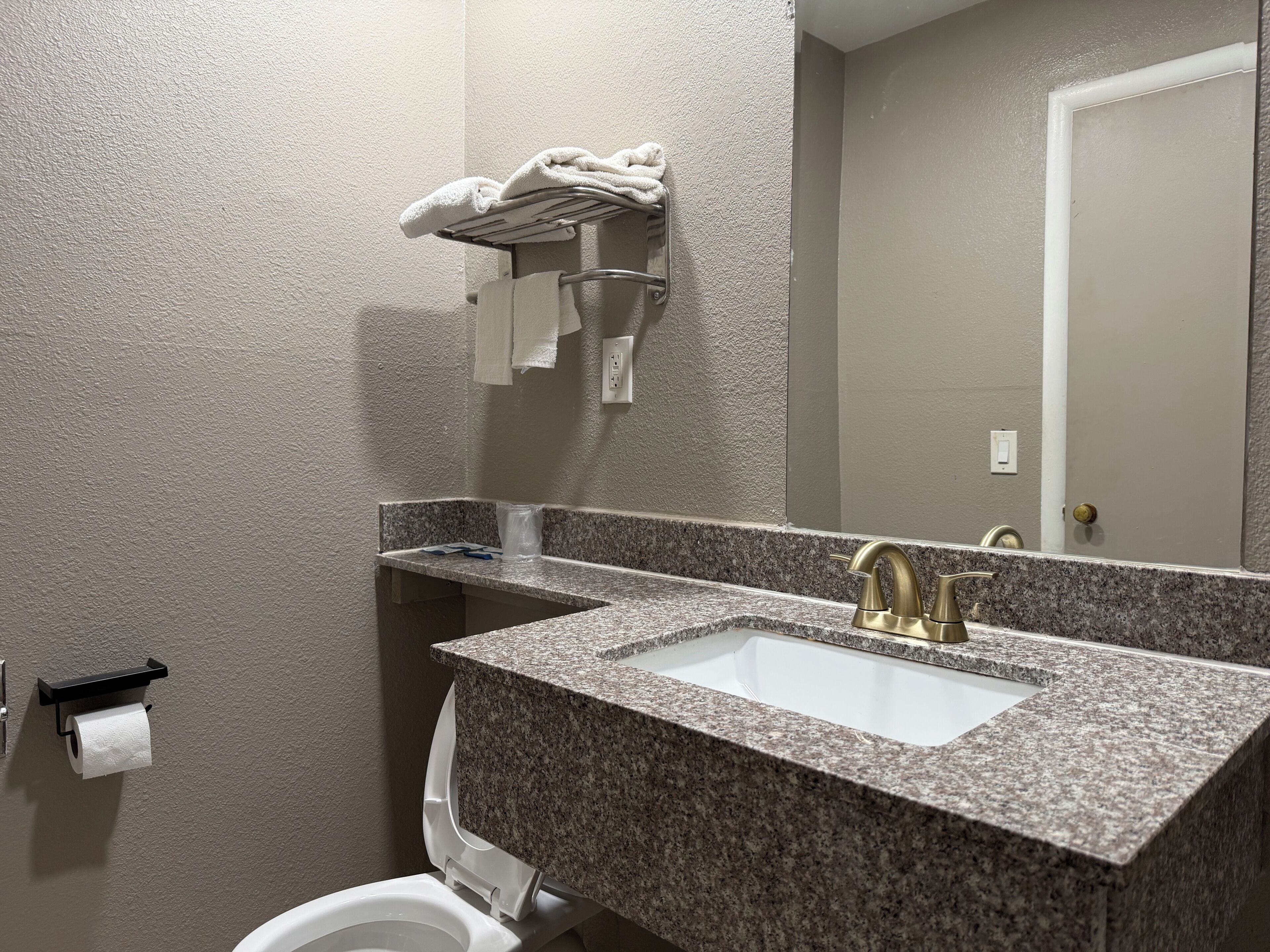 Un baño con lavamanos de encimera de granito, grifo dorado, toallero y un inodoro.