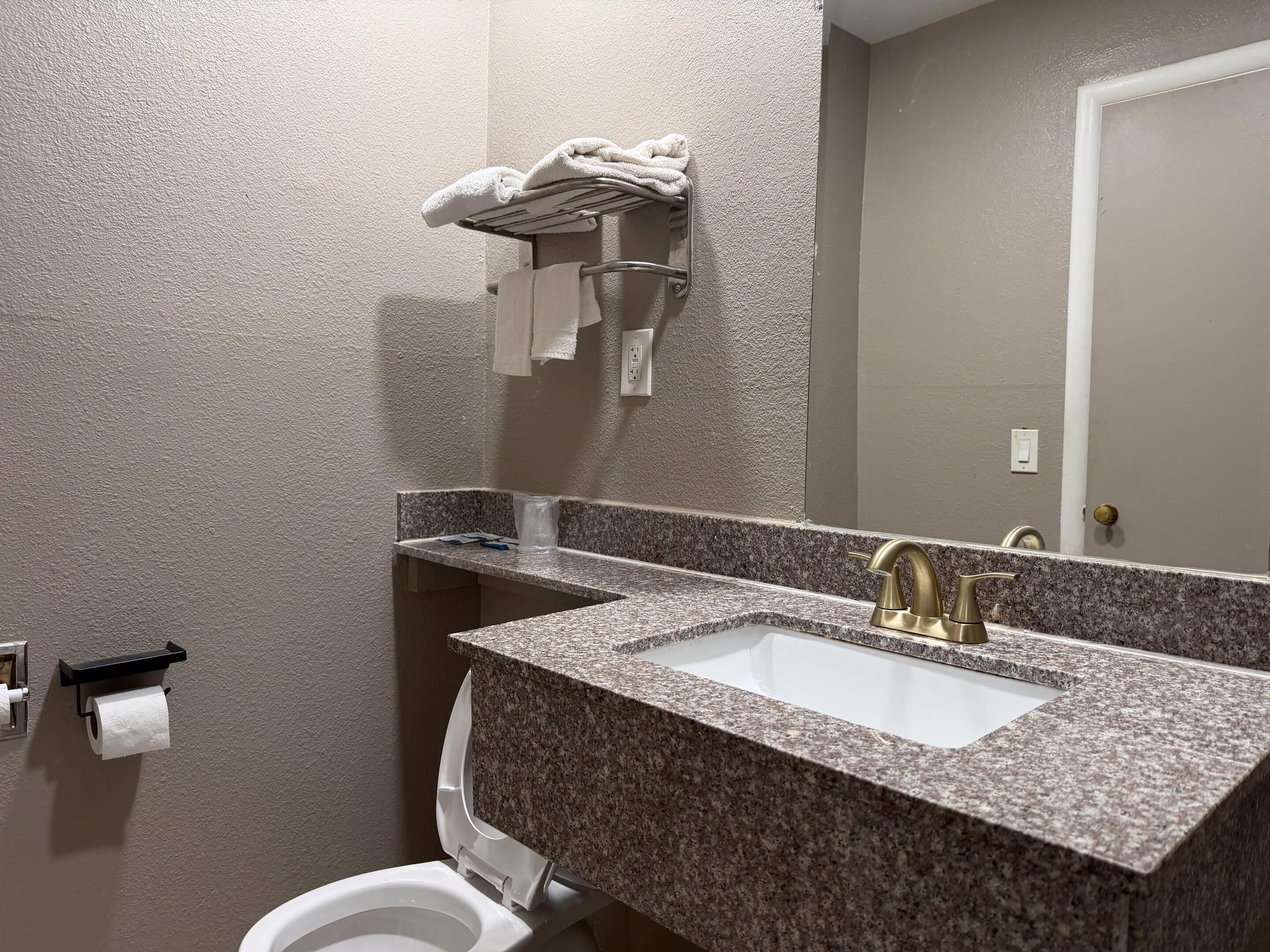 A bathroom with a granite countertop sink, a toilet, and a towel rack.