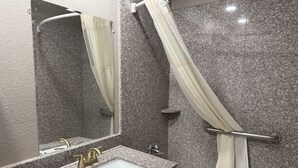 Un baño con lavamanos de encimera de granito, un espejo, cortina de ducha y bañera.