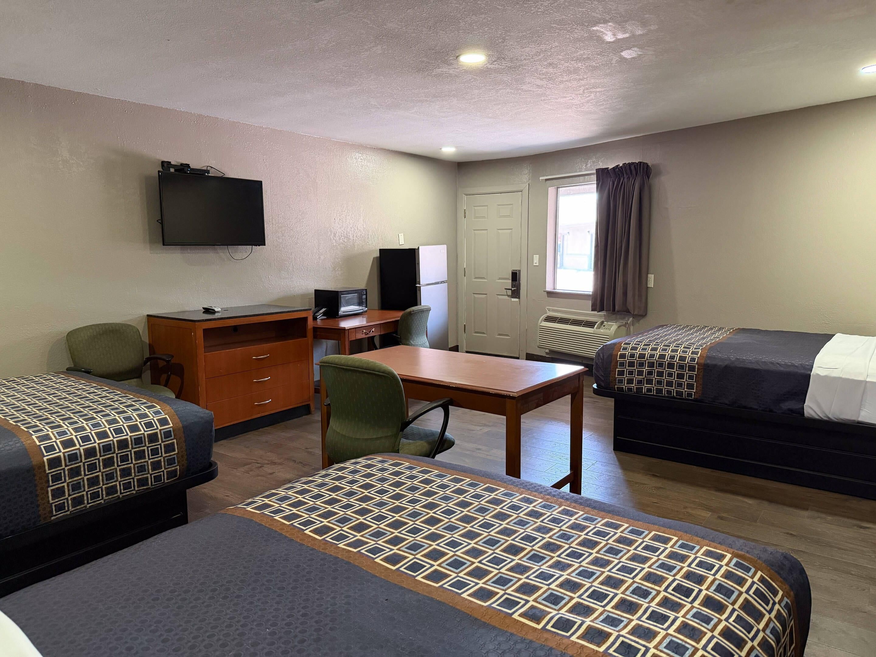 A hotel room with two beds, a desk, a chair, a television, and a door.