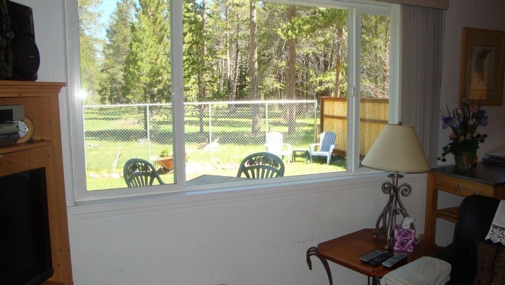 Une pièce dotée d’une grande fenêtre donnant sur une cour arrière clôtur ée, aménagée avec des chaises et une terrasse en bois.