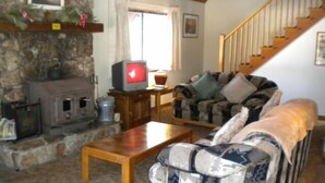 A cozy living room with a stone fireplace, a wooden coffee table, a patterned sofa, and a staircase. - 842 Cirugu (South Lake Tahoe)